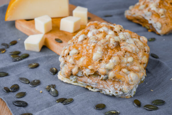Frisch gebackenes Kürbis-Käse-Brötchen mit goldbrauner Kruste und mit Käse überbacken, dazu Gouda und Kürbiskerne