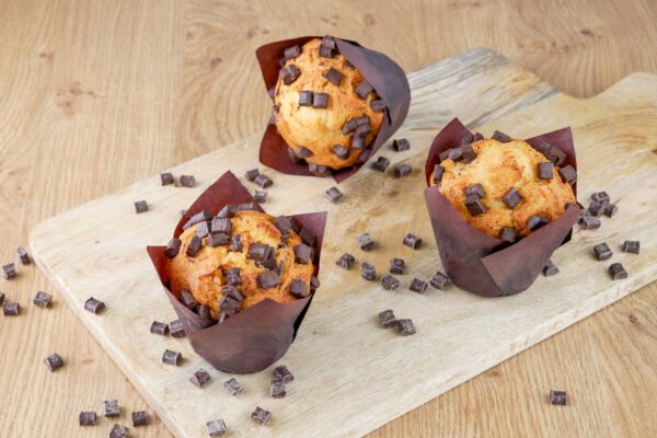 Muffins mit Schokoladenstückchen auf einem Brettchen umgeben von Schokostückchen